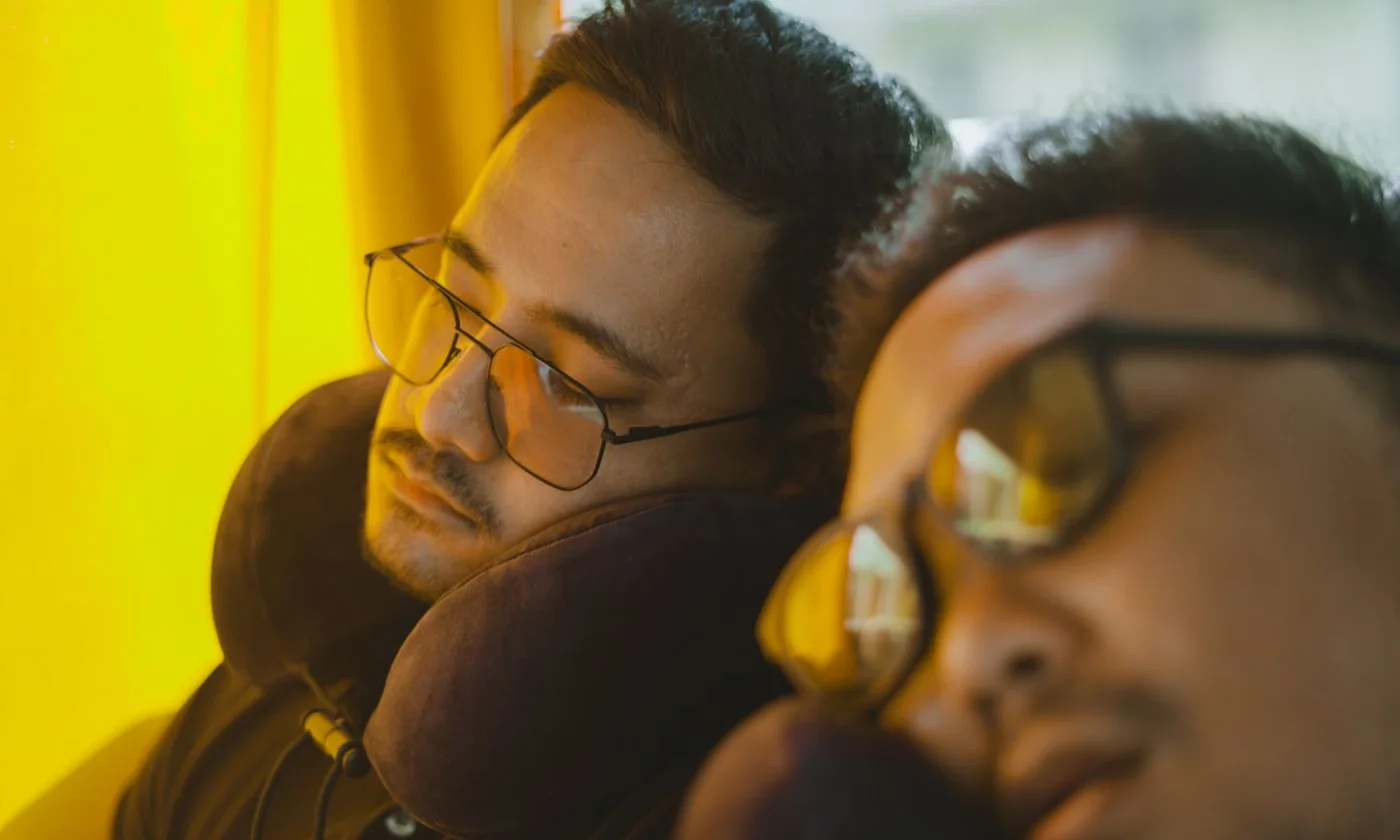 Two travelers resting with neck pillows on a bus